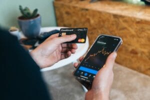Is Mastercard a Good Stock to Buy now? A person holding a Mastercard credit card and checking stock market performance on a smartphone, analyzing investment opportunities.